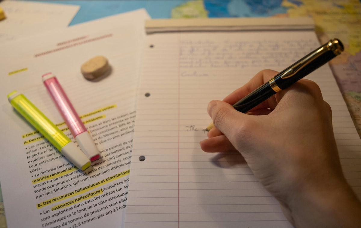 A student writing English notes in a notebook with a pen